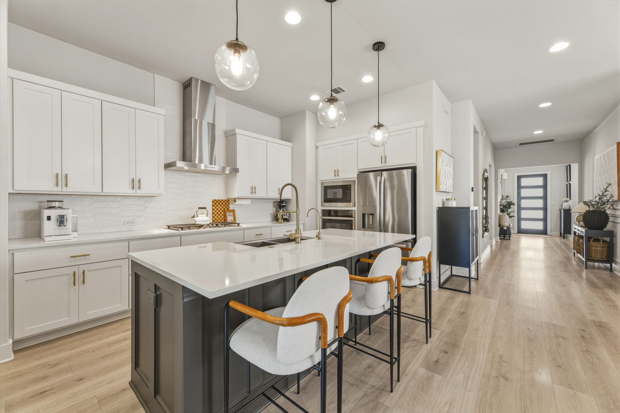 4505 Post Loop Round Rock, TX 78681 - Photo 16 of 40 Two tone kitchen with a center island with sink, a kitchen breakfast bar, dual tone cabinetry, pendant lighting, and light wood finished floors