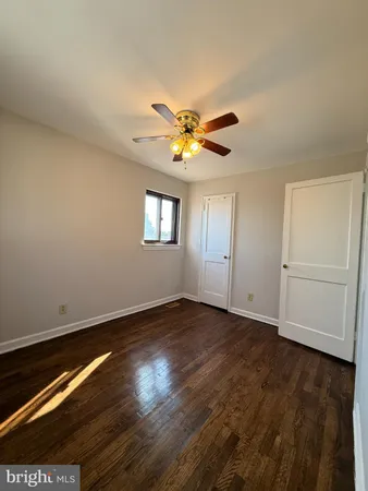 a view of an empty room with wooden floor and a ceiling fan