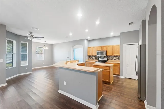 a kitchen with stainless steel appliances granite countertop a refrigerator a sink dishwasher a stove and white countertops with wooden floor