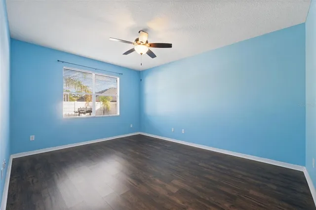 a view of an empty room with wooden floor and a ceiling fan