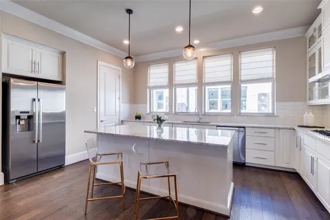 a kitchen with stainless steel appliances granite countertop a stove a sink dishwasher a refrigerator and white cabinets with wooden floor