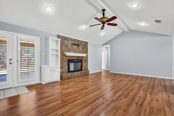 an empty room with wooden floor fireplace and windows