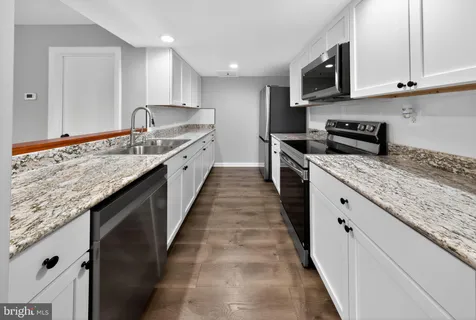 a large kitchen with granite countertop a sink and dishwasher a stove top oven with wooden floor