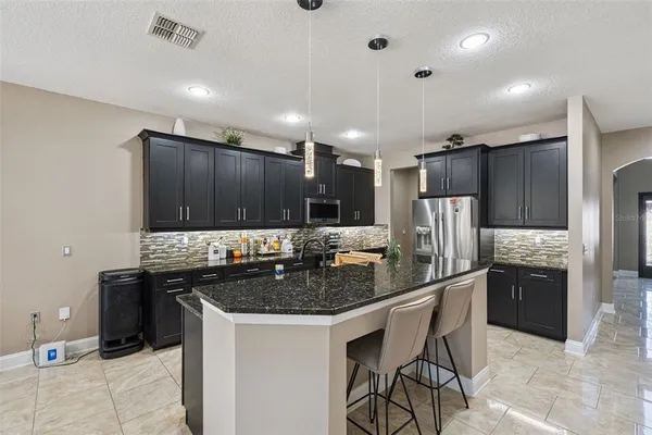 a kitchen with stainless steel appliances granite countertop a stove a sink a refrigerator and chairs