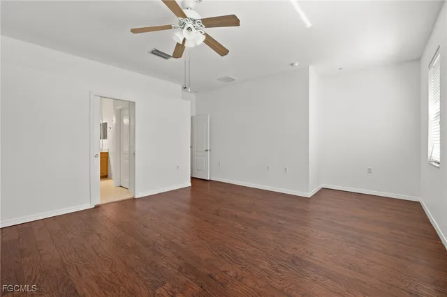 an empty room with wooden floor ceiling fan and windows