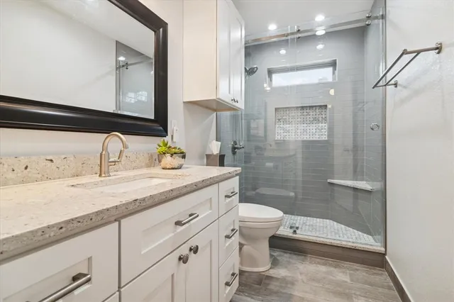 a bathroom with a granite countertop sink a toilet a mirror and shower