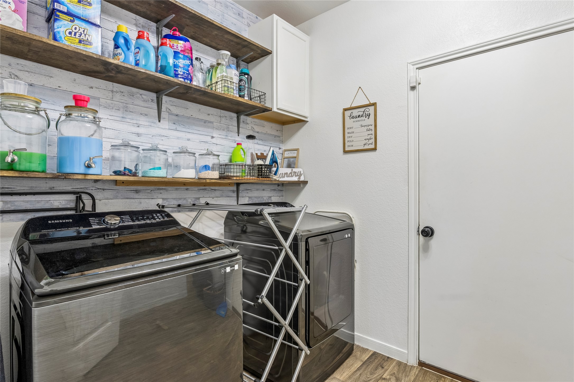 14409 Estuary Road Manor, TX 78653 - Photo 22 of 24 Dedicated laundry area featuring a wood-finish floor, white shiplap wall accent, and open wooden shelving
