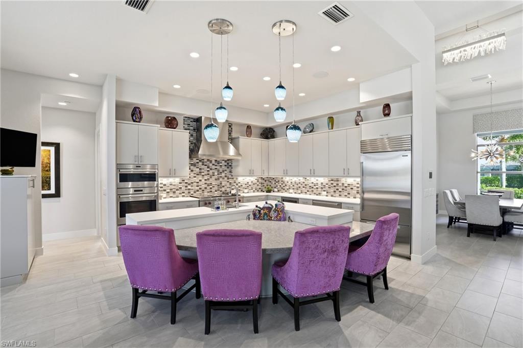 9177 Esplanade Boulevard Naples, FL 34119 - Photo 16 of 50 Kitchen with a breakfast bar area, backsplash, a center island with sink, appliances with stainless steel finishes, and wall chimney range hood