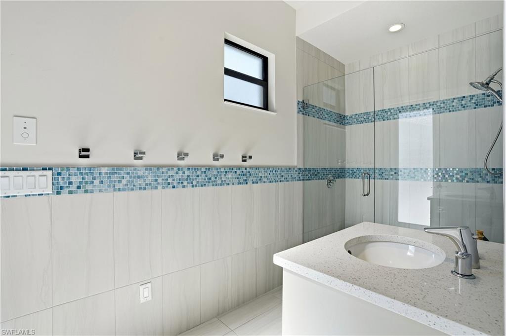 9177 Esplanade Boulevard Naples, FL 34119 - Photo 30 of 50 Bathroom with a shower stall, vanity, and tile walls