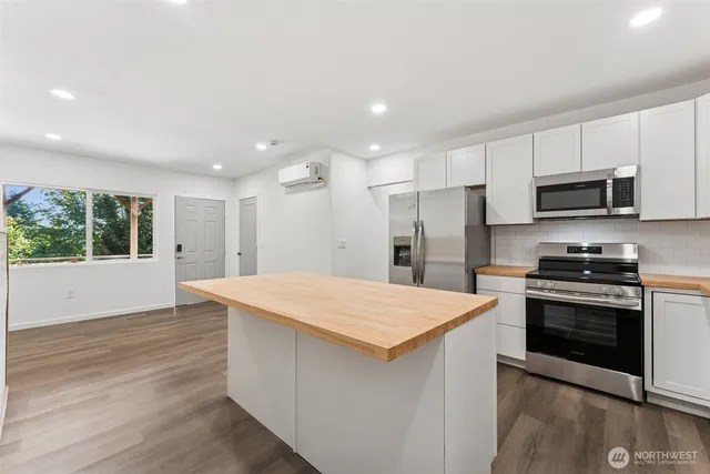 a kitchen with stainless steel appliances kitchen island a stove a refrigerator and a sink with wooden floor