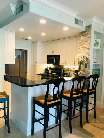 a kitchen with stainless steel appliances kitchen island granite countertop a dining table chairs and a refrigerator