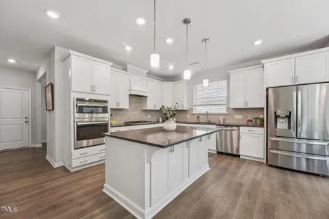 a kitchen with stainless steel appliances granite countertop a refrigerator a sink dishwasher a stove and white cabinets with wooden floor