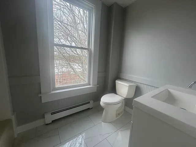 a white toilet sitting next to a window in a bathroom