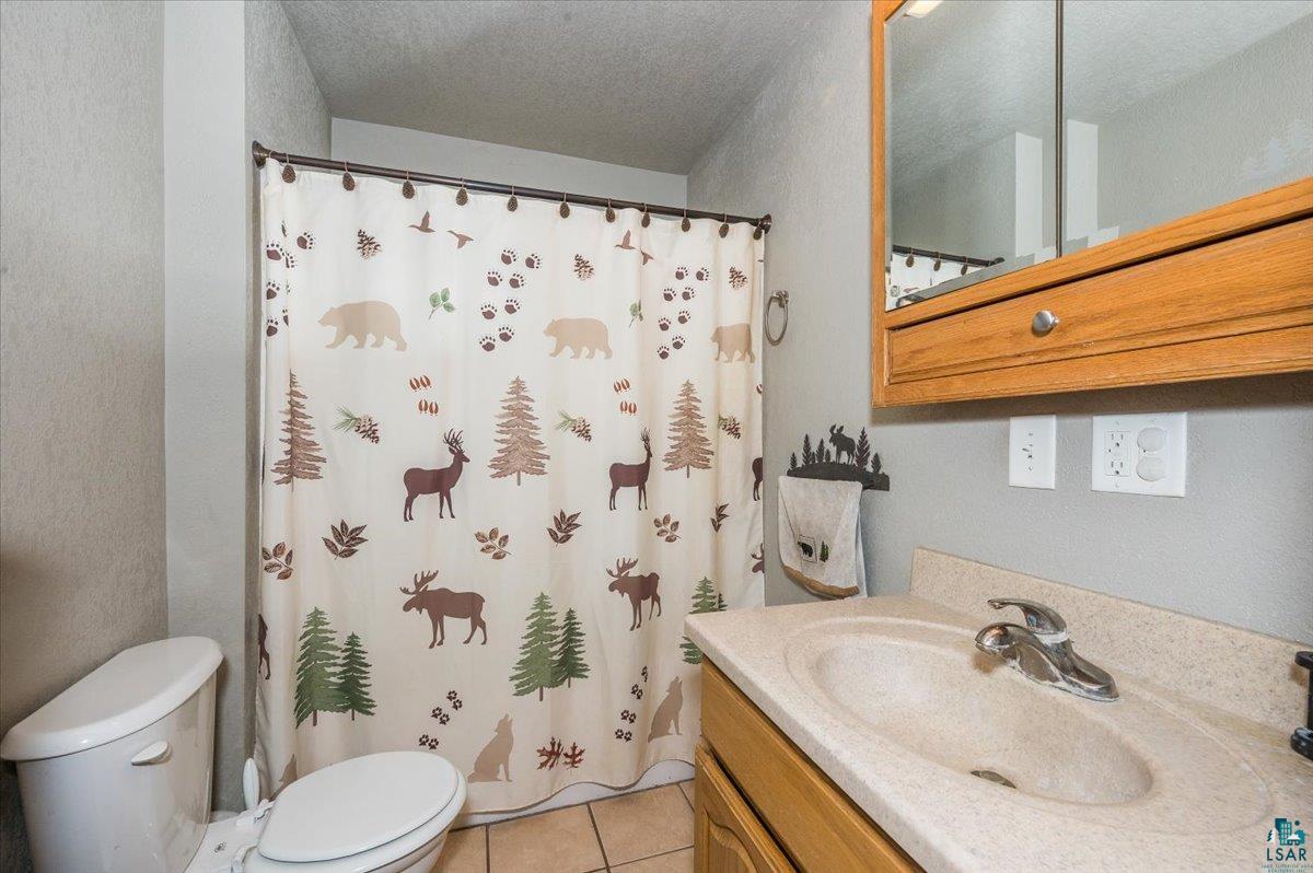 7702 East Rockmont Road Poplar, WI 54864 - Photo 13 of 22 Bathroom with a textured ceiling, toilet, tile patterned floors, a shower with curtain, and vanity