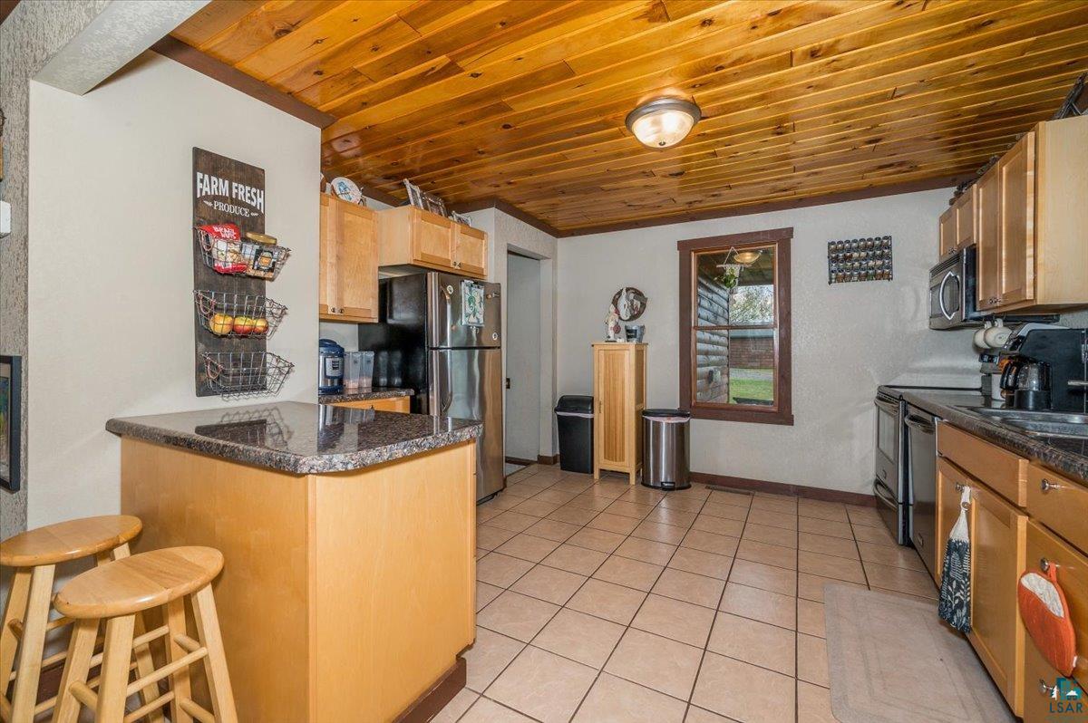 7702 East Rockmont Road Poplar, WI 54864 - Photo 6 of 22 Kitchen featuring a kitchen breakfast bar, kitchen peninsula, wooden ceiling, light tile patterned floors, and appliances with stainless steel finishes