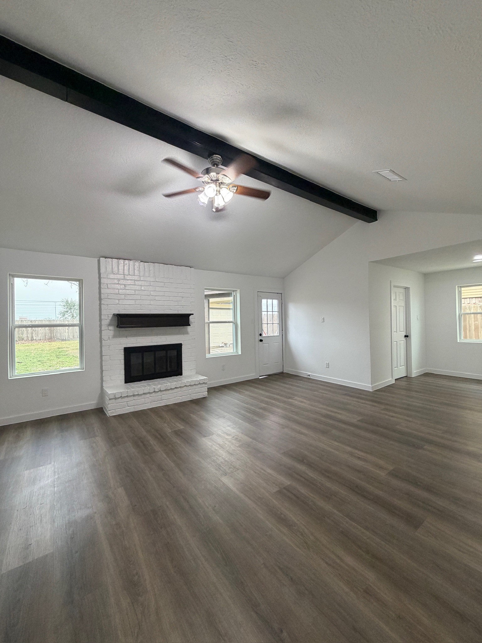 an empty room with wooden floor fireplace and windows