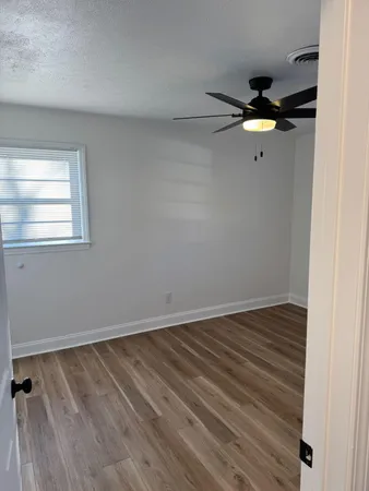 an empty room with wooden floor fan and windows