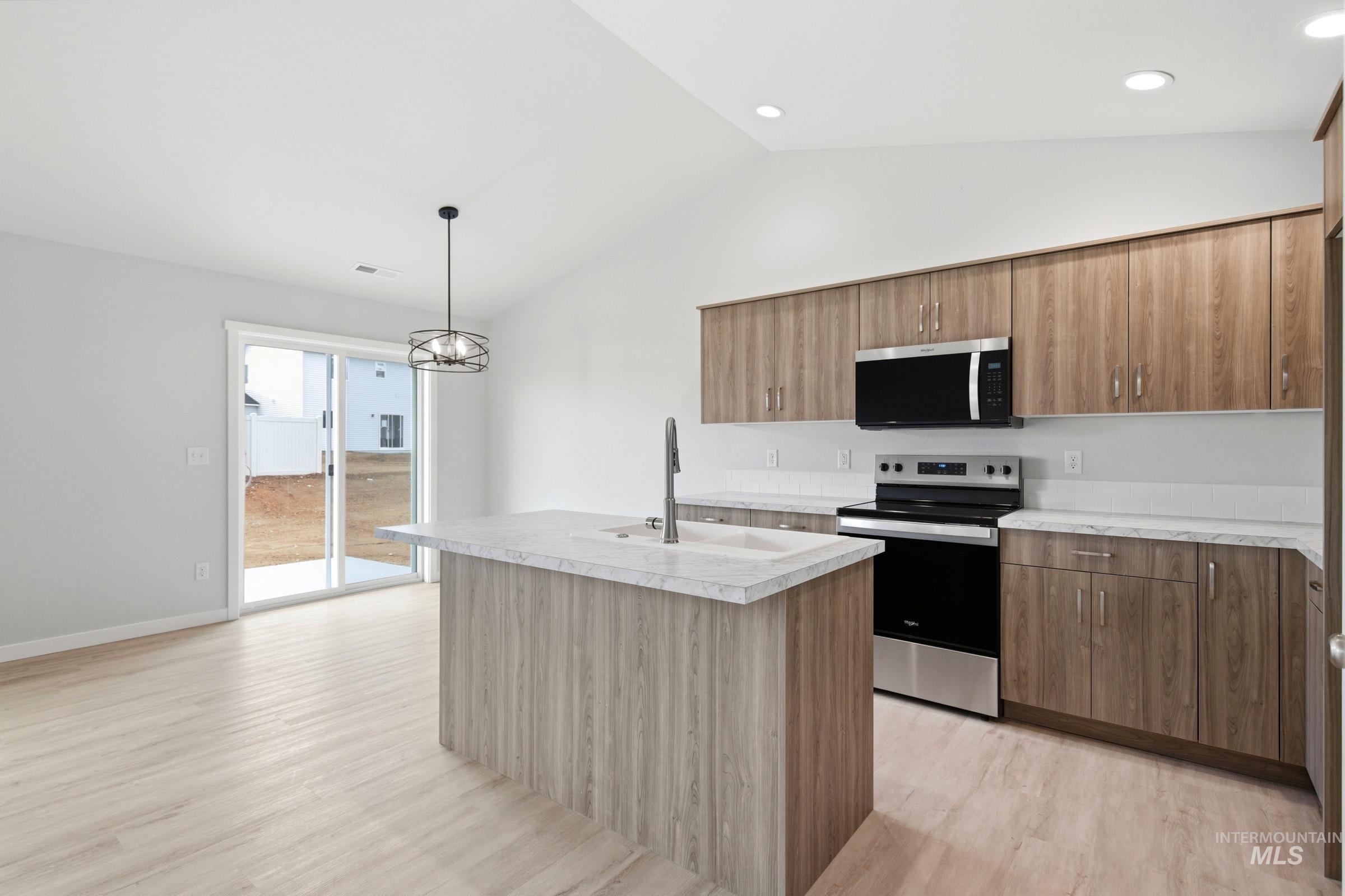 16632 North Shorthorn Loop Nampa, ID 83651 - Photo 4 of 17 Spacious kitchen featuring a central island with a sink, wood-finish flooring, full appliance suite including a stainless steel range and microwave, light-toned countertops, and extensive cabinetry