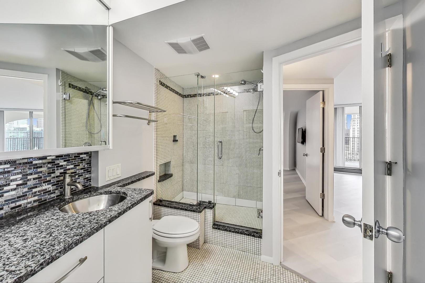 300 North State Street, Unit 4308 Chicago, IL 60654 - Photo 17 of 32 a bathroom with a granite countertop sink toilet mirror and shower