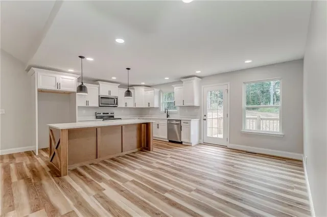 a large kitchen with stainless steel appliances kitchen island granite countertop a stove a sink a refrigerator and white cabinets with wooden floor
