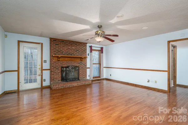an empty room with wooden floor fireplace and windows