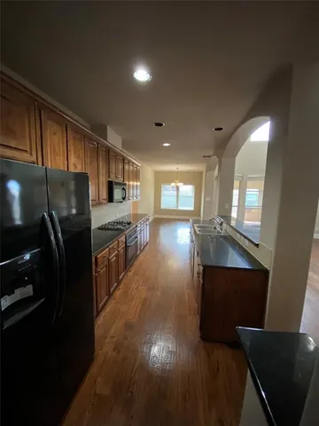 a kitchen with stainless steel appliances granite countertop a refrigerator a stove top oven and a sink with wooden floor