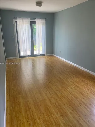 an empty room with wooden floor and windows with curtains