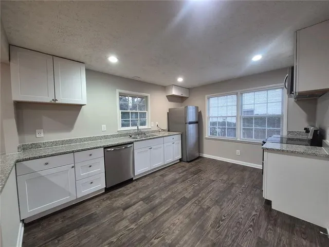 a large kitchen with granite countertop a stove a sink a refrigerator and white cabinets with wooden floor