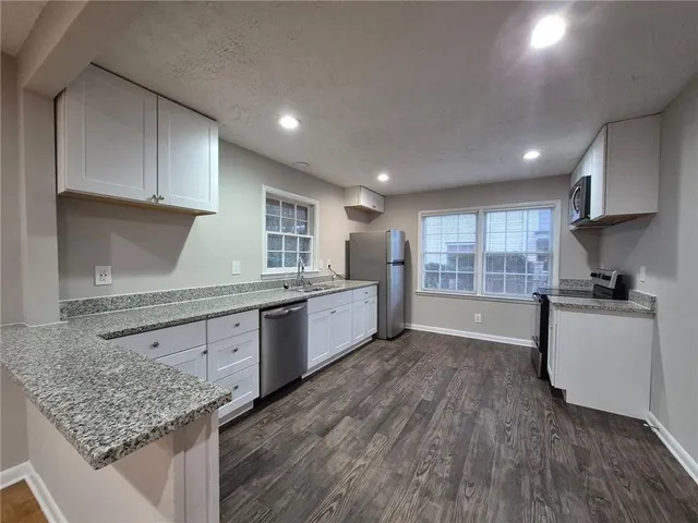a kitchen with stainless steel appliances granite countertop a sink dishwasher a stove and a refrigerator with wooden floor