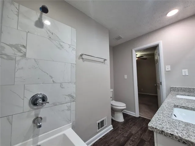 a bathroom with a granite countertop sink a toilet and shower