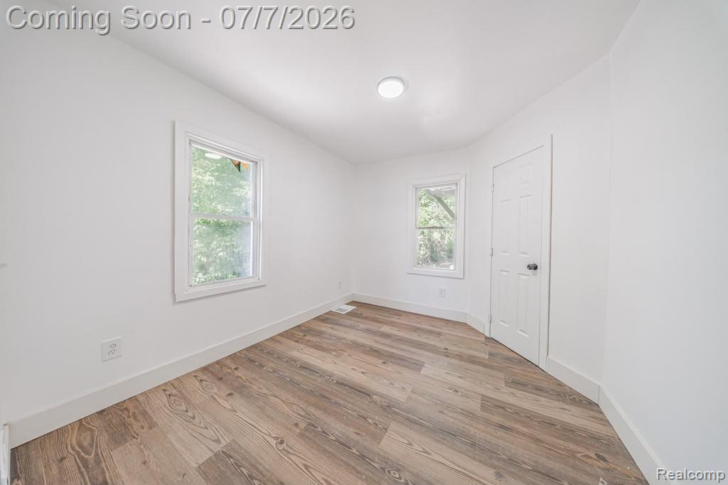 18486 Trinity Street Detroit, MI 48219 - Photo 16 of 19 Room featuring wood-finish flooring, two window openings, a white paneled door, and a flush-mount ceiling light fixture