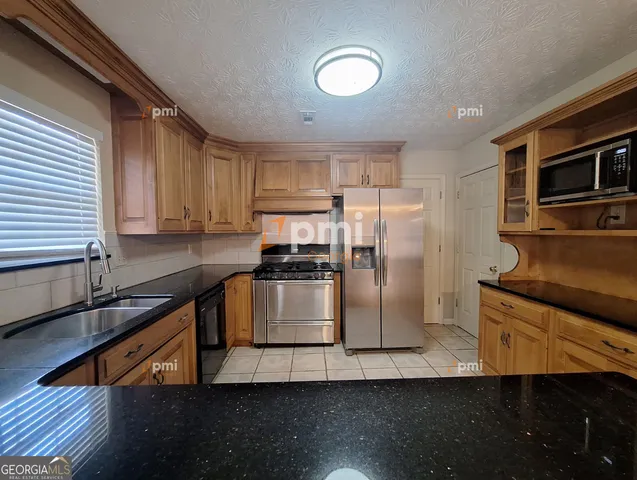 a kitchen with stainless steel appliances granite countertop a refrigerator a stove and a sink with wooden floors