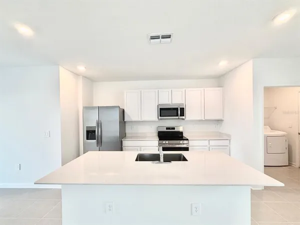 a large white kitchen with kitchen island a sink stainless steel appliances and cabinets