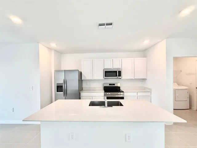 a large white kitchen with kitchen island a sink stainless steel appliances and cabinets