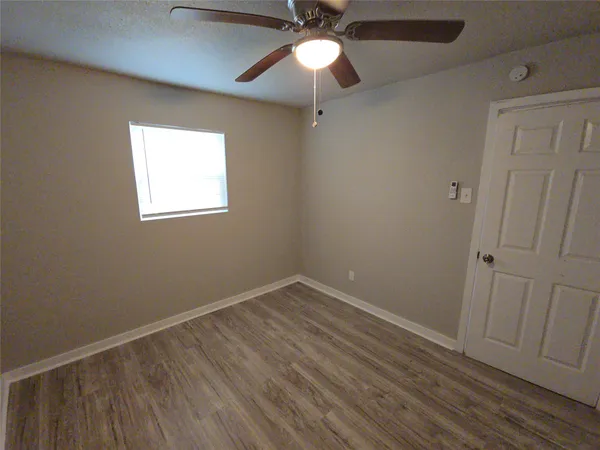an empty room with wooden floor fan and window