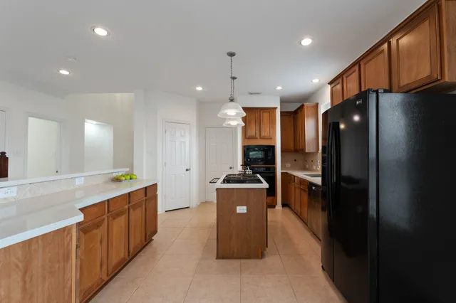 a kitchen with stainless steel appliances kitchen island granite countertop a refrigerator a stove and a sink with wooden cabinets