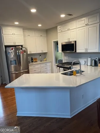 a kitchen with stainless steel appliances a sink a stove a microwave a refrigerator a center island and cabinets