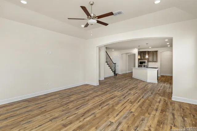 an empty room with wooden floor a ceiling fan and kitchen view