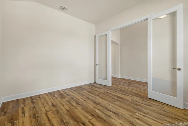 a view of an empty room with wooden floor and a bathroom