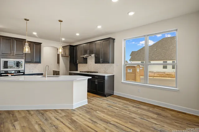 a large kitchen with stainless steel appliances granite countertop a stove top oven a sink dishwasher a refrigerator and white cabinets with wooden floor