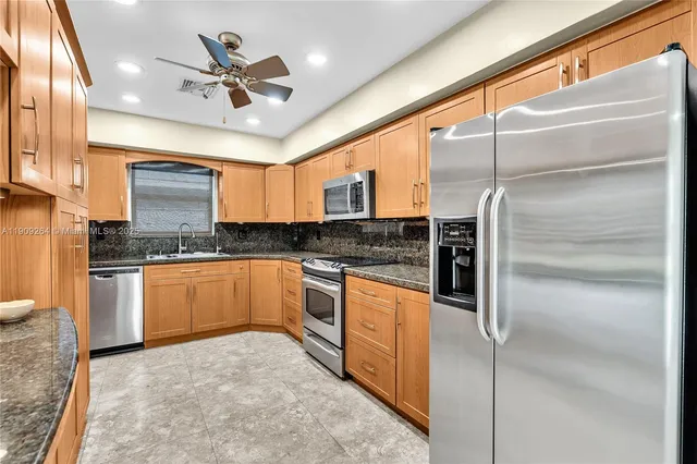 a kitchen with stainless steel appliances granite countertop a refrigerator a sink and white cabinets