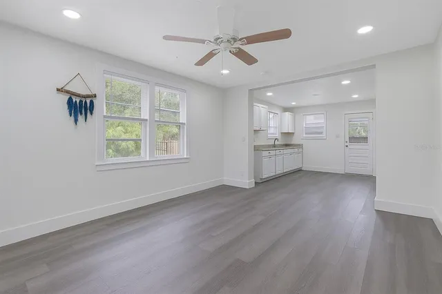 an empty room with wooden floor a ceiling fan and windows