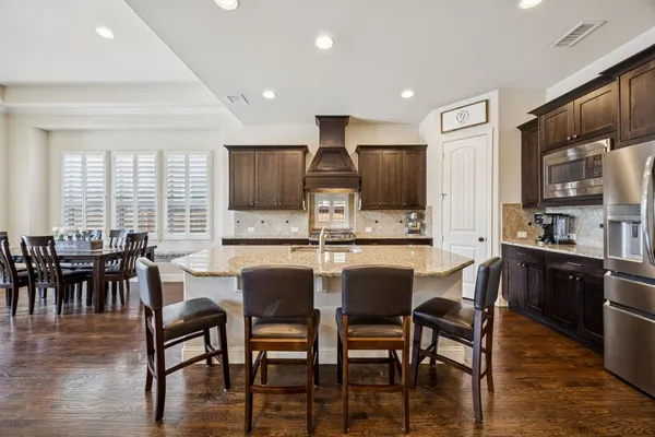 a kitchen with stainless steel appliances kitchen island granite countertop a dining table chairs and a refrigerator