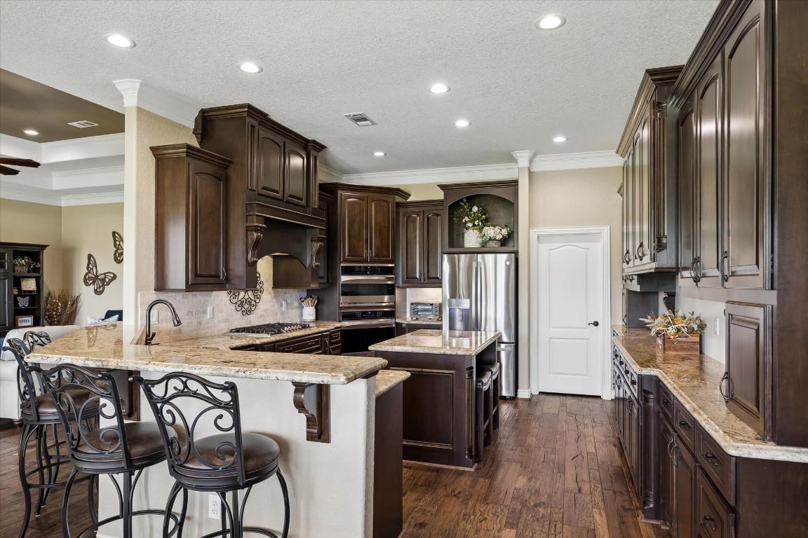 17703 Cedarhill Drive Rosharon, TX 77583 - Photo 11 of 47 A chef's dream kitchen showcasing rich dark custom cabinetry, gleaming granite countertops, a gas cooktop, stainless steel appliances, a breakfast bar peninsula, and a generous walk-in pantry — all flowing seamlessly into the living room for effortless entertaining.