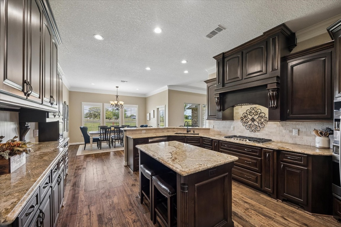 17703 Cedarhill Drive Rosharon, TX 77583 - Photo 12 of 47 The expansive kitchen opens beautifully to the dining area, highlighting abundant counter space, a center island, custom hood vent, stone tile backsplash, and hardwood floors — a true heart-of-the-home layout designed for the way families actually live.