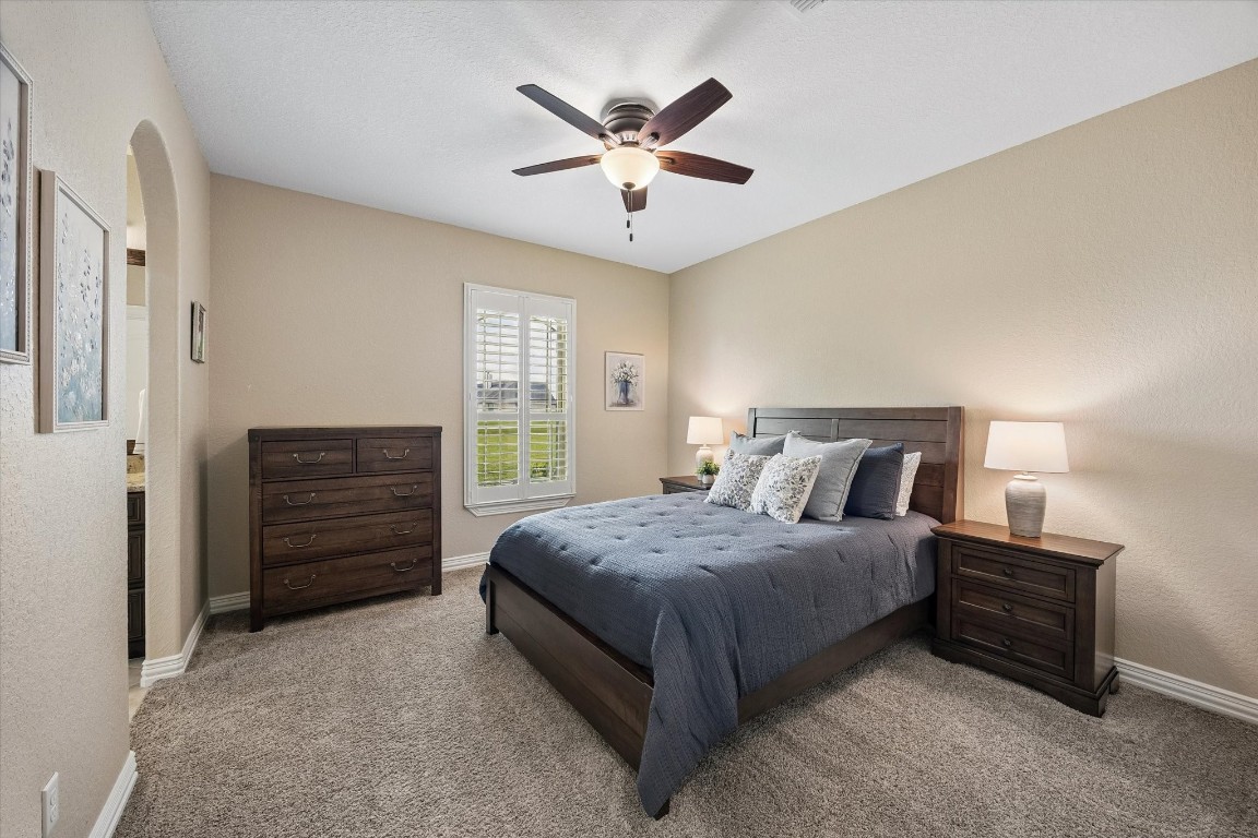 17703 Cedarhill Drive Rosharon, TX 77583 - Photo 19 of 47 A generously sized secondary bedroom with plush carpet, plantation shutters, ceiling fan, and an elegant arched doorway — comfortable and inviting for family or guests alike.