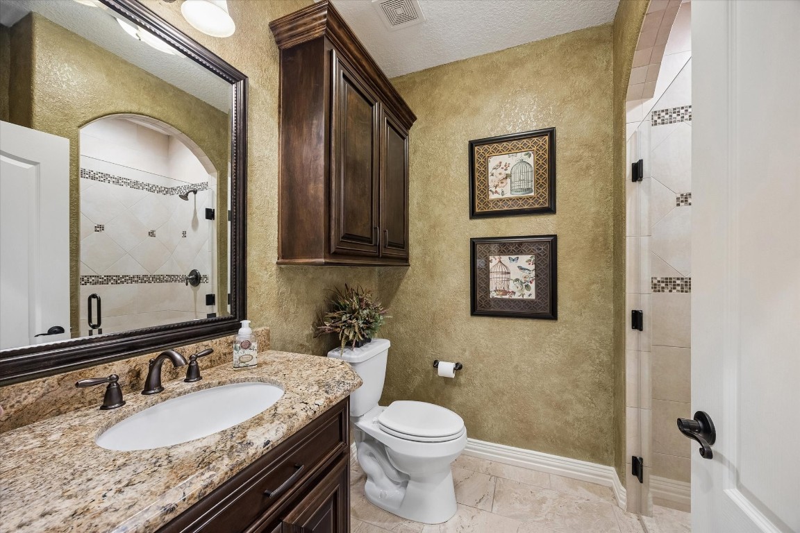 17703 Cedarhill Drive Rosharon, TX 77583 - Photo 23 of 47 The private ensuite bath serving the 4th bedroom wing features rich Venetian-textured walls, custom dark cabinetry with upper storage, granite countertops, oil-rubbed bronze fixtures, a framed mirror, and a beautifully tiled walk-in shower with mosaic accent border — a fully appointed bath that completes this home's private guest or multigenerational suite.