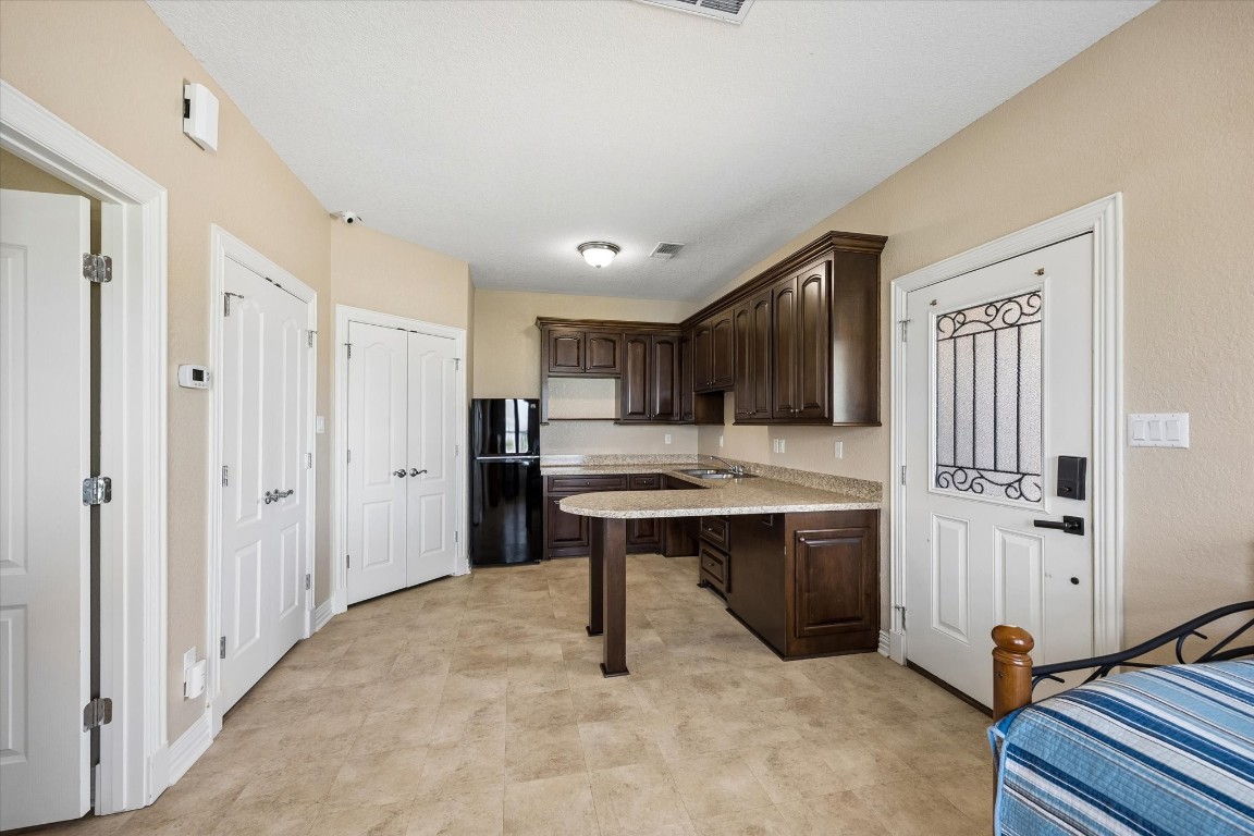 17703 Cedarhill Drive Rosharon, TX 77583 - Photo 35 of 47 The fully equipped casita kitchen features custom dark cabinetry, granite countertops, a peninsula breakfast bar, refrigerator, and a dedicated closet pre-plumbed for a washer and dryer — delivering true independent living convenience in a beautifully finished space.
