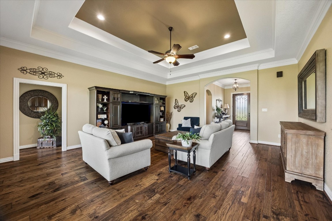 17703 Cedarhill Drive Rosharon, TX 77583 - Photo 8 of 47 The expansive living room stuns with a dramatic tray ceiling, crown molding, recessed lighting, and rich hardwood floors — all flowing naturally from the foyer through elegant arched doorways, creating an open and connected living experience.