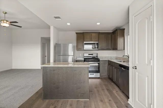 a kitchen with stainless steel appliances granite countertop a refrigerator a stove top oven a sink and dishwasher with wooden floor